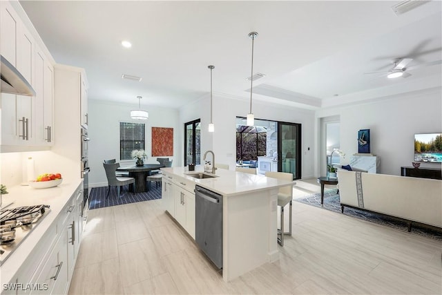 kitchen with white cabinets, appliances with stainless steel finishes, hanging light fixtures, and an island with sink