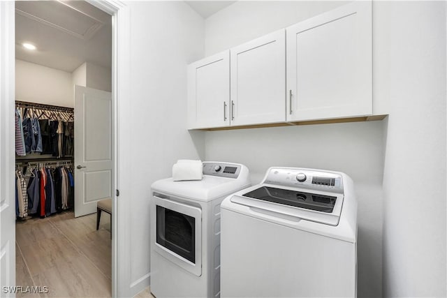 clothes washing area featuring cabinets, light hardwood / wood-style floors, and washing machine and clothes dryer