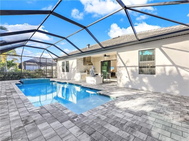 view of swimming pool featuring glass enclosure, ceiling fan, a patio area, and exterior kitchen