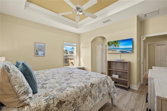 bedroom featuring a tray ceiling, a closet, ceiling fan, and light hardwood / wood-style flooring