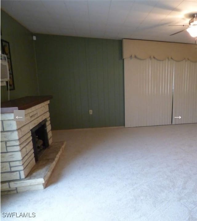 unfurnished living room with carpet, a stone fireplace, and ceiling fan