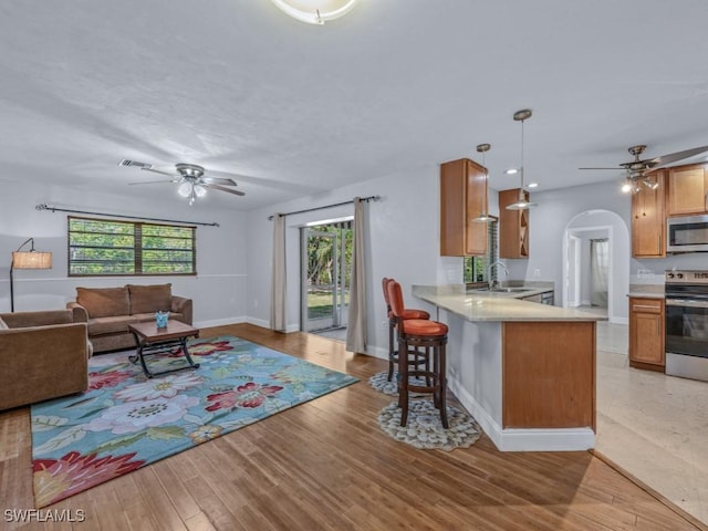 kitchen featuring kitchen peninsula, a kitchen breakfast bar, stainless steel appliances, pendant lighting, and light hardwood / wood-style floors