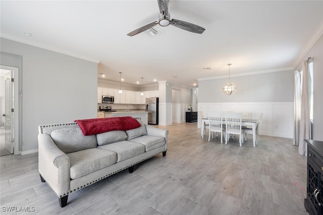 living area with a wainscoted wall, ceiling fan with notable chandelier, light wood-style flooring, and crown molding