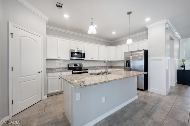 kitchen with an island with sink, appliances with stainless steel finishes, hanging light fixtures, white cabinetry, and a sink