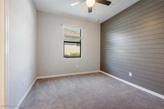 carpeted spare room with wood walls, baseboards, and ceiling fan