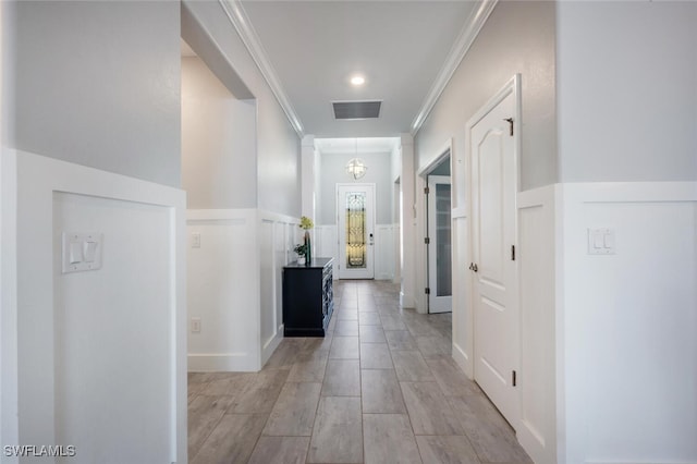 corridor with a wainscoted wall, ornamental molding, visible vents, and a decorative wall