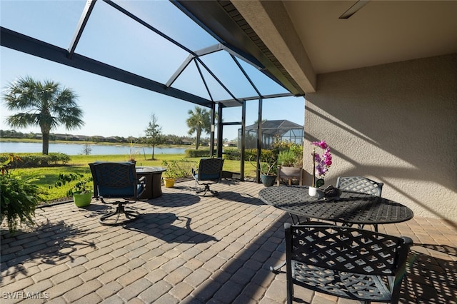 view of patio featuring glass enclosure, outdoor dining area, and a water view