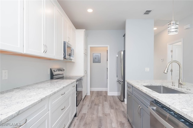 kitchen with sink, light wood-type flooring, appliances with stainless steel finishes, light stone counters, and white cabinetry