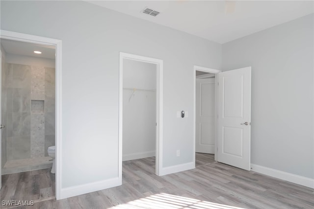 unfurnished bedroom with a walk in closet, ensuite bathroom, light hardwood / wood-style flooring, and a closet