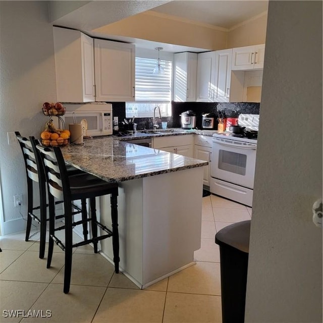 kitchen with kitchen peninsula, dark stone counters, white appliances, sink, and white cabinetry