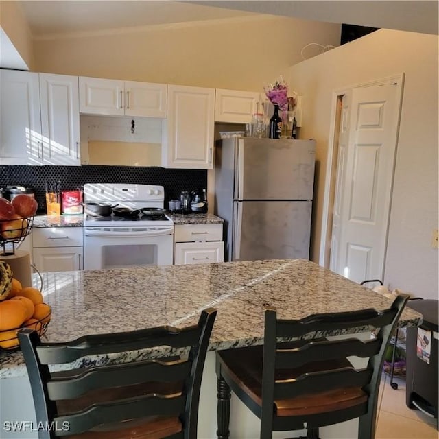 kitchen with a kitchen bar, white range, white cabinetry, and stainless steel refrigerator