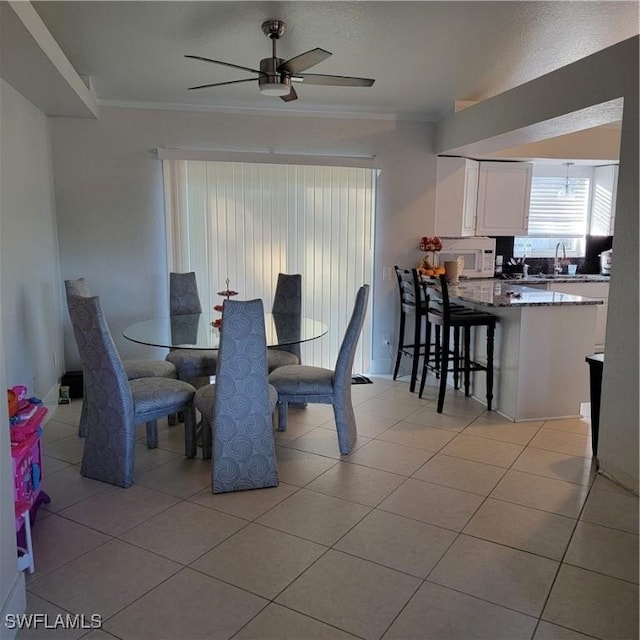 dining space featuring ceiling fan, light tile patterned flooring, sink, and crown molding