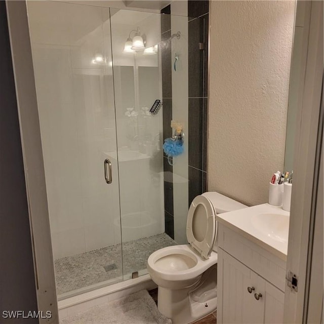 bathroom with toilet, a shower stall, vanity, and a textured wall