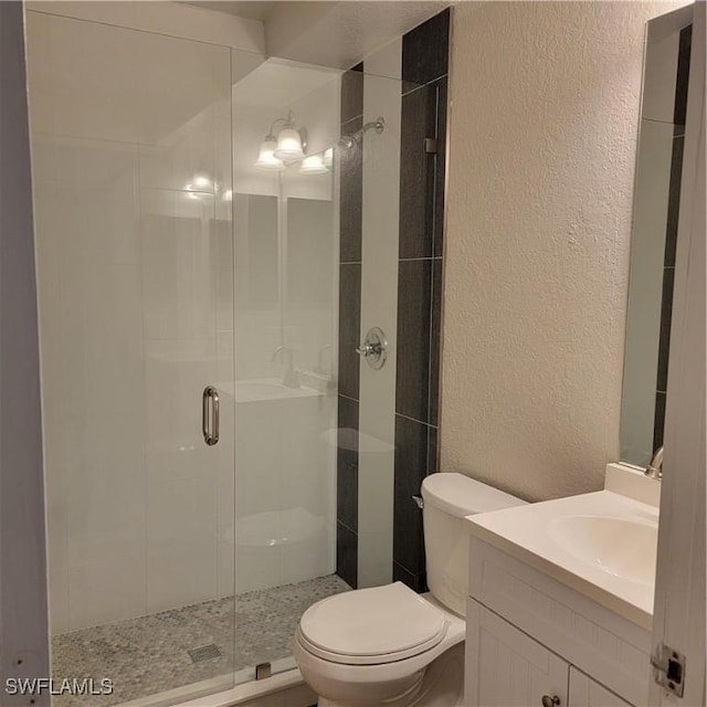 bathroom featuring a textured wall, vanity, a shower stall, and toilet