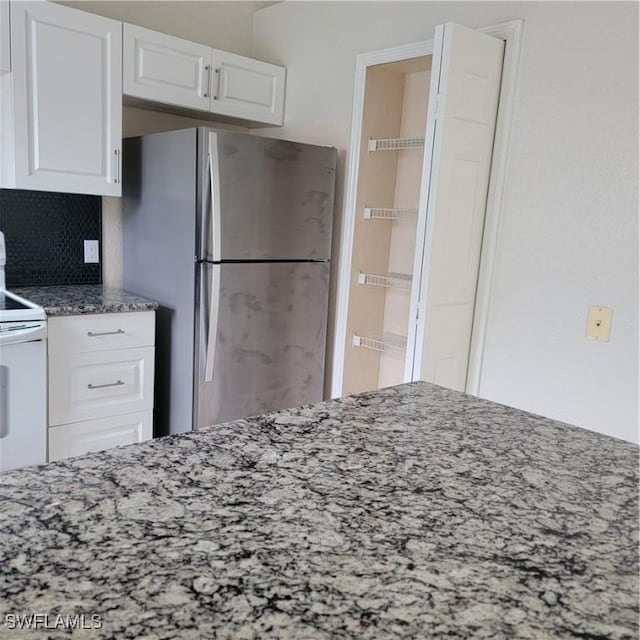 kitchen featuring stone counters, decorative backsplash, white range with electric stovetop, white cabinetry, and stainless steel refrigerator