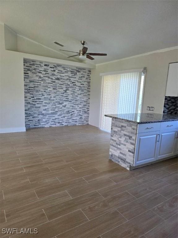 kitchen featuring crown molding, wood finish floors, ceiling fan, and dark stone countertops
