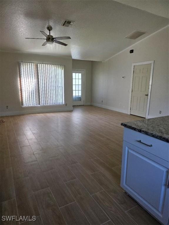 unfurnished living room featuring dark wood-type flooring, visible vents, ceiling fan, and a textured ceiling