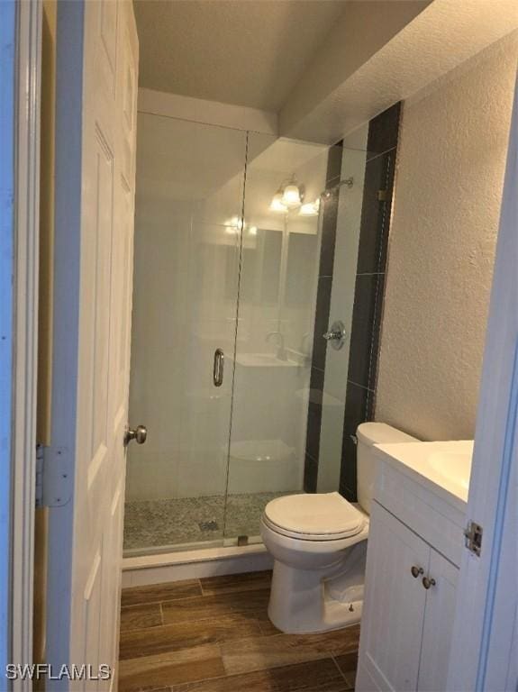 bathroom featuring a textured wall, toilet, wood tiled floor, vanity, and a shower stall