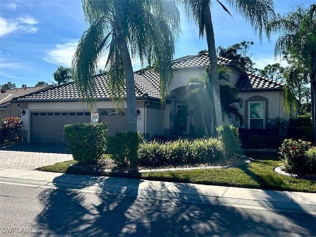 mediterranean / spanish house featuring a garage, a tiled roof, decorative driveway, and stucco siding