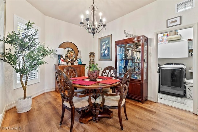 dining space with a wealth of natural light, light hardwood / wood-style floors, washer / clothes dryer, and an inviting chandelier