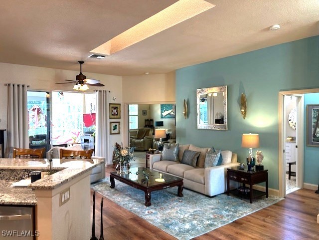 living area featuring baseboards, visible vents, ceiling fan, wood finished floors, and a textured ceiling