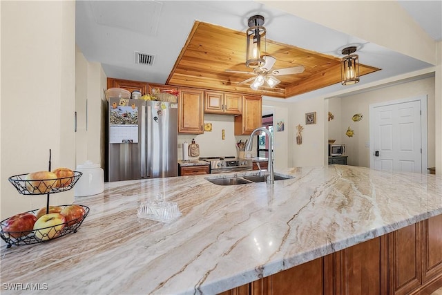 kitchen featuring light stone countertops, stainless steel fridge, a raised ceiling, ceiling fan, and sink