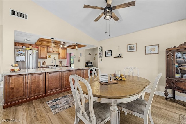 dining area featuring ceiling fan, sink, light hardwood / wood-style floors, and vaulted ceiling