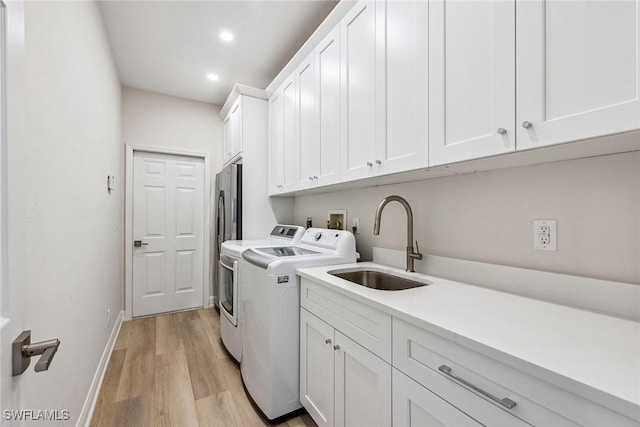 clothes washing area featuring cabinets, washing machine and clothes dryer, sink, and light wood-type flooring