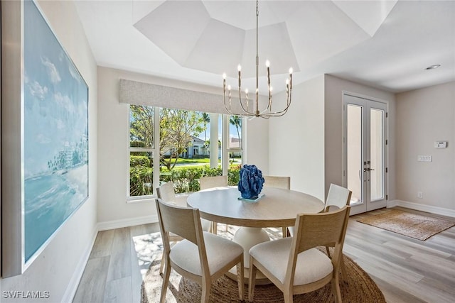 dining room featuring an inviting chandelier, light hardwood / wood-style floors, and a raised ceiling