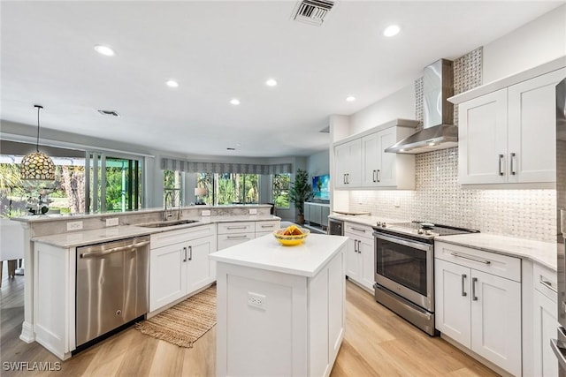 kitchen with white cabinetry, sink, a center island, stainless steel appliances, and wall chimney exhaust hood