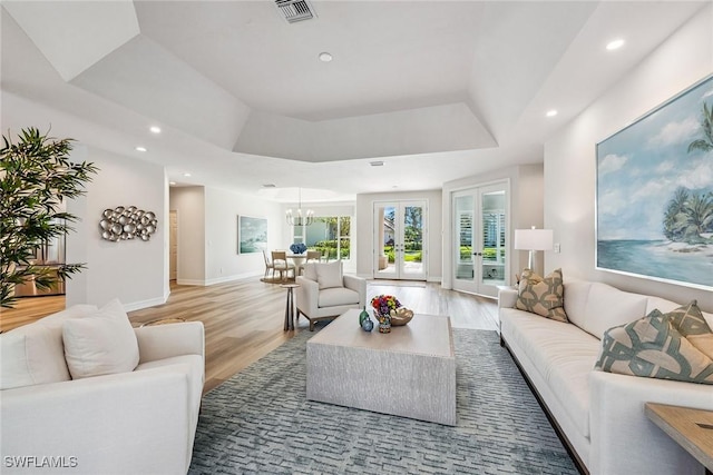 living room with an inviting chandelier, hardwood / wood-style floors, a tray ceiling, and french doors