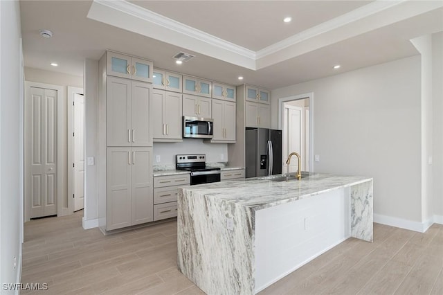 kitchen featuring appliances with stainless steel finishes, a center island with sink, light stone counters, and a raised ceiling