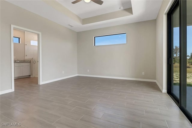 empty room with a raised ceiling, ceiling fan, and light hardwood / wood-style floors