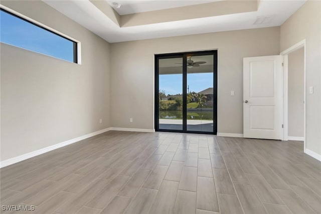 empty room featuring a tray ceiling, plenty of natural light, and light hardwood / wood-style floors