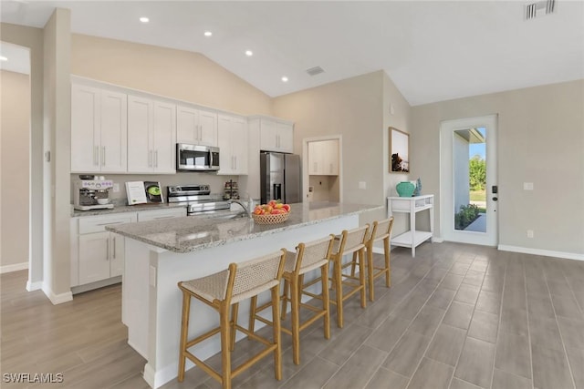 kitchen featuring white cabinetry, an island with sink, stainless steel appliances, and lofted ceiling