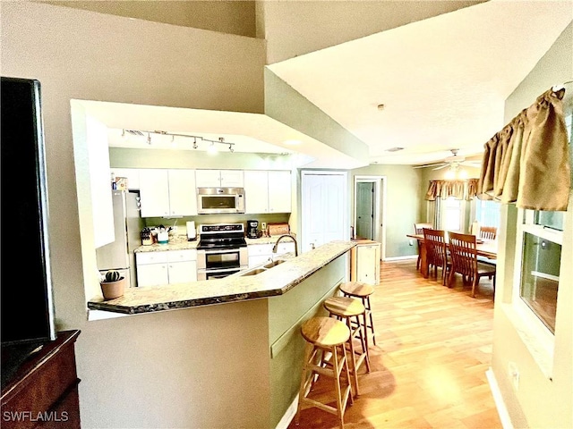 kitchen featuring white cabinets, a kitchen breakfast bar, sink, light wood-type flooring, and appliances with stainless steel finishes