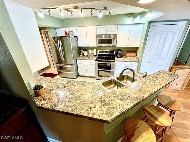 kitchen featuring white cabinets, sink, appliances with stainless steel finishes, a kitchen bar, and kitchen peninsula