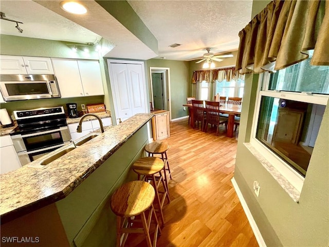 kitchen with a kitchen bar, rail lighting, a textured ceiling, stainless steel appliances, and white cabinetry