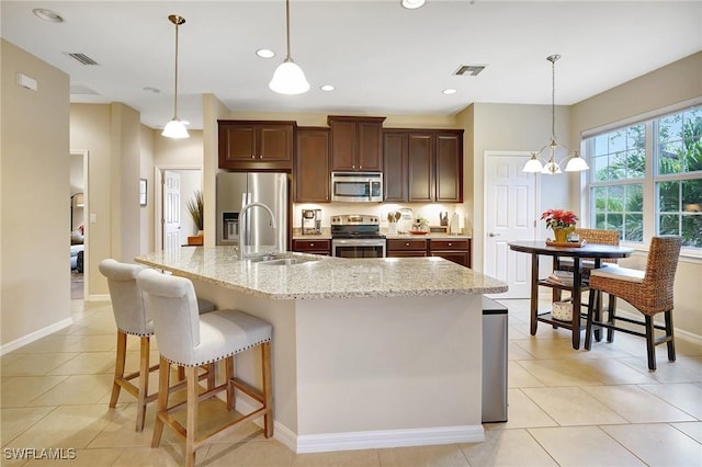 kitchen featuring stainless steel appliances, a kitchen island with sink, sink, light tile patterned floors, and decorative light fixtures