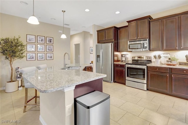 kitchen with hanging light fixtures, sink, appliances with stainless steel finishes, and an island with sink