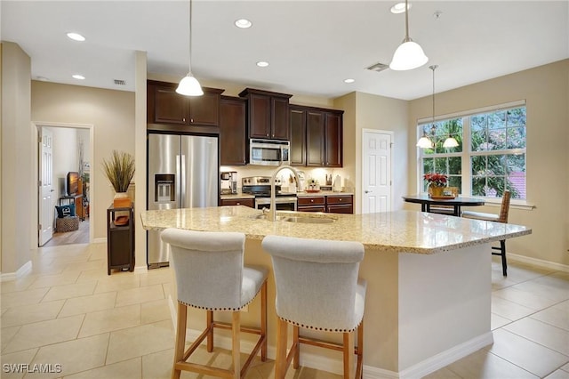 kitchen with sink, hanging light fixtures, an island with sink, light stone counters, and stainless steel appliances