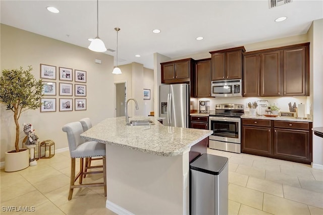 kitchen with stainless steel appliances, sink, decorative light fixtures, a center island with sink, and a breakfast bar area