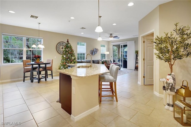 kitchen with light stone countertops, sink, pendant lighting, and a center island with sink