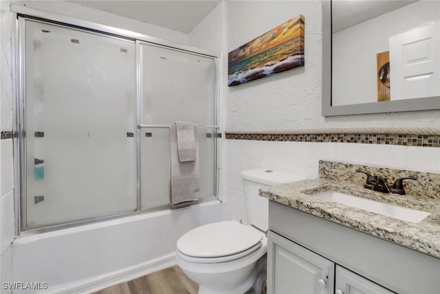 full bathroom with vanity, toilet, combined bath / shower with glass door, and tile walls