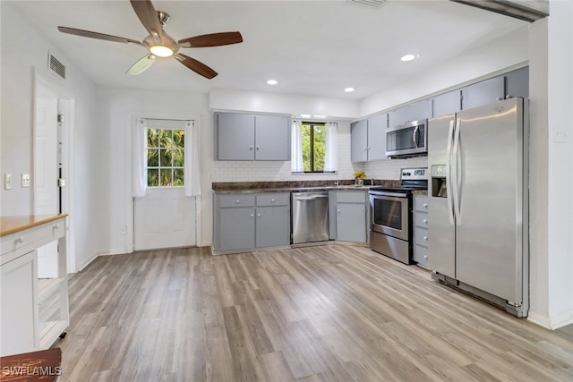 kitchen with gray cabinetry, decorative backsplash, a healthy amount of sunlight, and appliances with stainless steel finishes