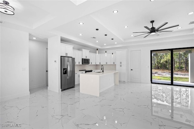 kitchen with a kitchen island with sink, white cabinets, ceiling fan, a tray ceiling, and stainless steel appliances