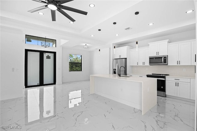 kitchen with ceiling fan, hanging light fixtures, stainless steel appliances, a center island with sink, and white cabinets