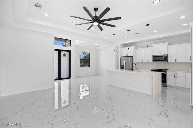 kitchen featuring appliances with stainless steel finishes, a tray ceiling, a kitchen island with sink, ceiling fan, and white cabinets