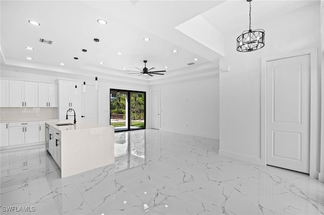 kitchen featuring a center island with sink, ceiling fan with notable chandelier, sink, a tray ceiling, and white cabinetry