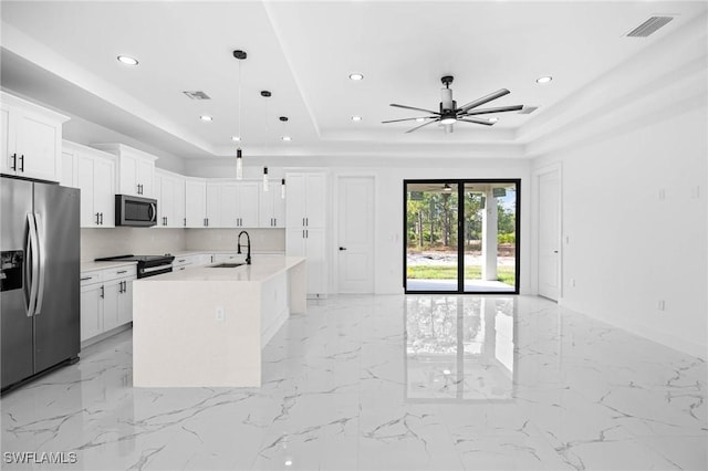 kitchen featuring appliances with stainless steel finishes, decorative light fixtures, white cabinetry, and a kitchen island with sink